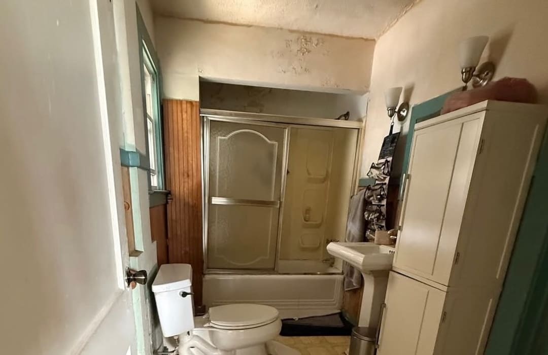 Before: worn bathroom with a framed tub door and pedestal sink in Wayne